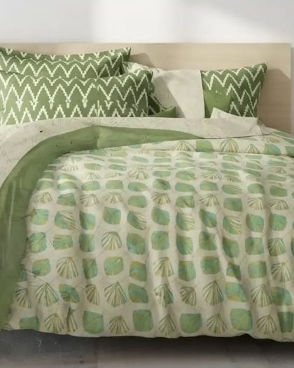 Green leaf print bedsheet set with matching geometric pillow covers in a stylish modern bedroom.