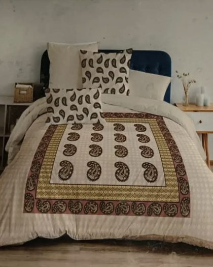 Beige paisley printed cotton bedspread with maroon border and matching cushion covers on blue upholstered bed