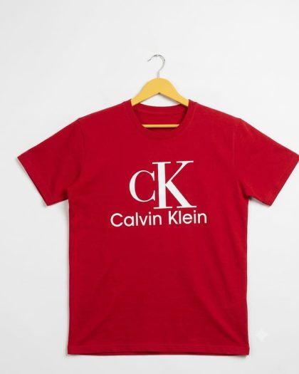 Red Calvin Klein boys’ short-sleeve crew-neck T-shirt with white CK logo, displayed on a hanger against a white background